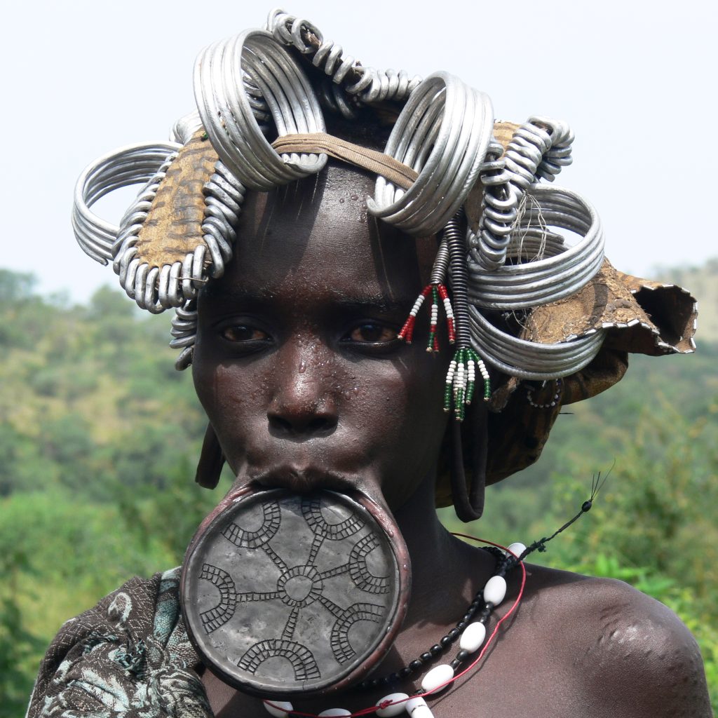 Mursi tribe woman with traditional lip plate in Ethiopia Hamar tribe cultural dance in Southern Ethiopia Scenic landscape of the Omo Valley region Traditional tribal market in Jinka Ethiopia Karo tribe body painting near the Omo River Travelers enjoying the 7-Day Omo Valley Tour in Ethiopia